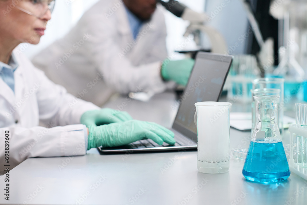 Cropped shot of scientists working with equipment in laboratory, focus on medical glassware on desk with reacting chemicals Cropped shot of scientists working with equipment in laboratory, focus on medical glassware on desk with reacting chemicals