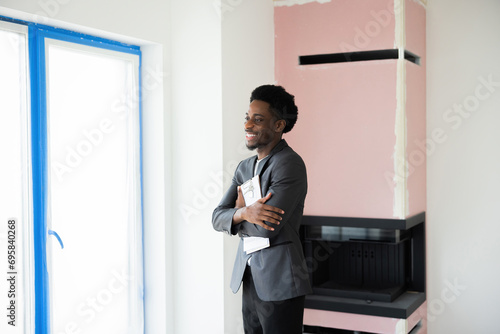 Confident delighted african american dark skinned man holding house plan in hands looking straiht.