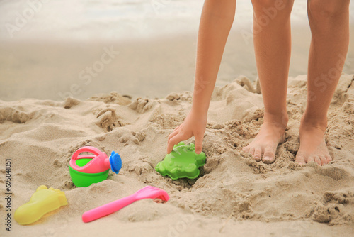 Little girl playing with plastic toys on sandy beach, closeup