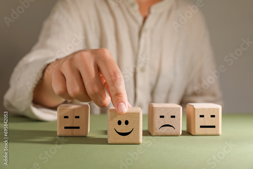 Choice concept. Woman choosing wooden cube with happy emoticon among others at green table, closeup