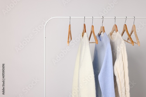 Rack with different warm sweaters on light background. Space for text