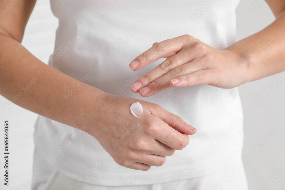 Woman applying cosmetic cream onto hand on blurred background, closeup