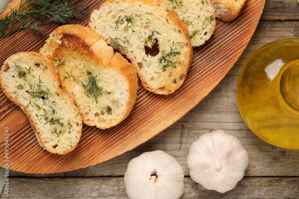 Tasty baguette with garlic, dill and oil on wooden table, flat lay Tasty baguette with garlic, dill and oil on wooden table, flat lay