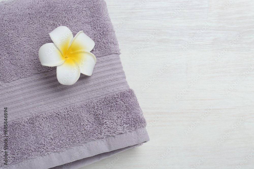 Violet terry towel and plumeria flower on light wooden table, top view. Space for text Violet terry towel and plumeria flower on light wooden table, top view. Space for text