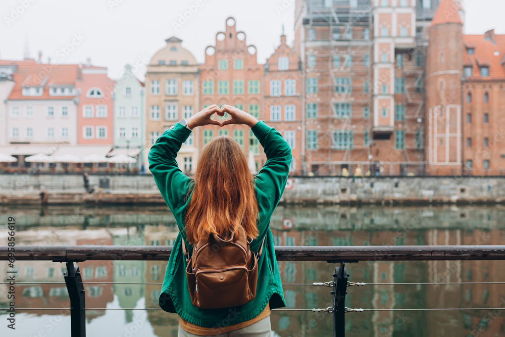 Adventure women making by hands in shape of love heart. Attractive young female tourist is exploring new city. Traveling Europe in autumn, rainy day, rear view