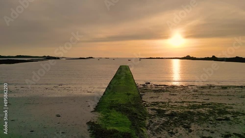 Sunset over Cobo Bay Guernsey slow flight over jetty and beach at mid tide into the sunset with boats at anchor and golden sky photo