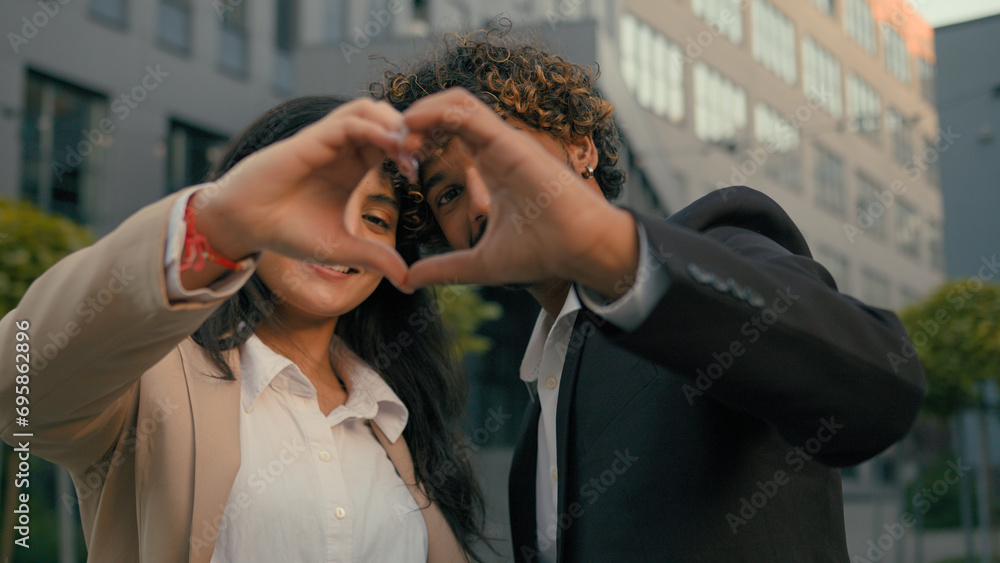 Indian couple Arabian business man businessman woman businesswoman corporate colleagues coworkers partners showing heart shape with hands fingers at camera in city near office building love support