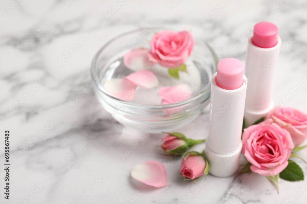 Lip balms, bowl with water and roses on white marble table, closeup Lip balms, bowl with water and roses on white marble table, closeup
