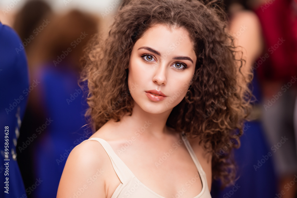 girl model. a young girl of model appearance with curly hair and a light T-shirt stands against the background of people and the podium girl model. a young girl of model appearance with curly hair and a light T-shirt stands against the background of people and the podium