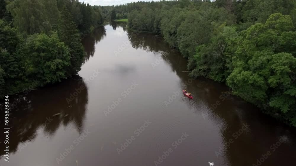 People with red canoes moving into the distance. Active holidays in nature. Camera rises slowly upwards. Travelling and local tourism in Estonia. High angle view People with red canoes moving into the distance. Active holidays in nature. Camera rises slowly upwards. Travelling and local tourism in Estonia. High angle view