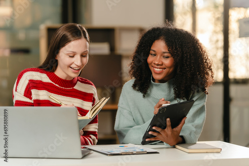 Caucasian and an African American student smiling and looking at a tablet, possibly collaborating on a university project.