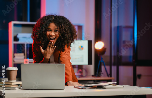 African-American woman with curly hair, wearing an orange blazer, surprise at the computer in an office setting.