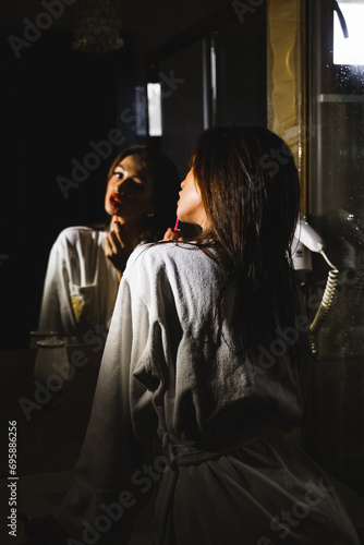 Young woman in a bathrobe paints her lips in the bathroom.Hotel holiday concept