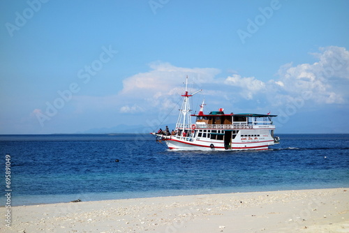 White and red Boat Cruisin next to the beach in Indonesia with coulds in the backround photo
