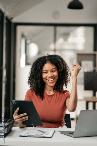Fotografi Excited african, american woman sitting at table feeling happy black woman overjoyed accepting mail at laptop promoted at home surprised girl reading good news