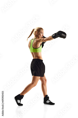 Jab punch. Young sportive woman with muscularly fit body practicing boxing isolated over white background. Concept of sport, active and healthy lifestyle, strength and endurance, body care