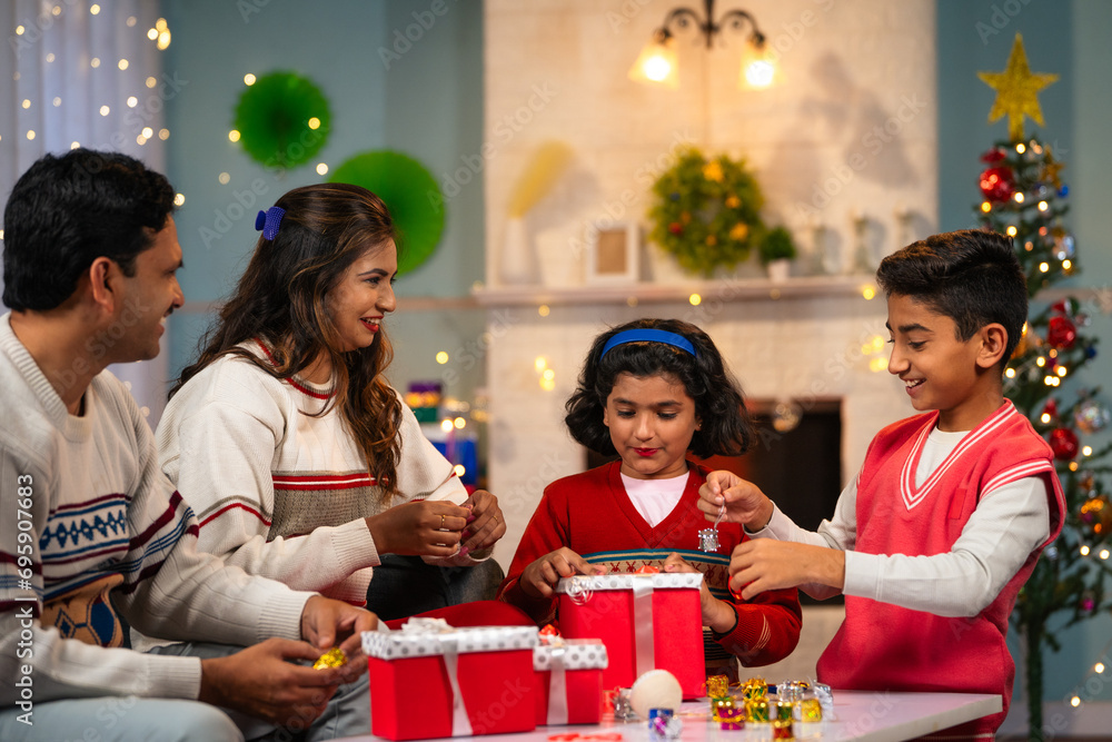 happy Indian Sibling kids with parents preparing Christmas gifts and decorations at home - concept of festive planning, holiday celebration and family bonding happy Indian Sibling kids with parents preparing Christmas gifts and decorations at home - concept of festive planning, holiday celebration and family bonding