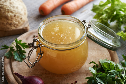 A jar of chicken bone broth or soup with fresh vegetables photo