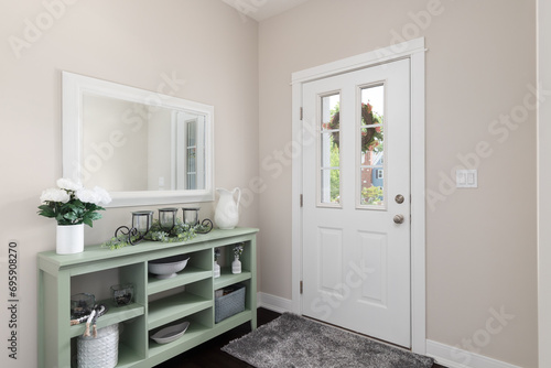 A cozy entryway with brown walls  a green console table with decorations  and a white front door.