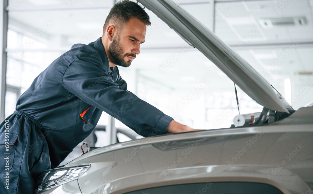 Focused on fixing the vehicle. Car repairman is in the garage with automobile Focused on fixing the vehicle. Car repairman is in the garage with automobile