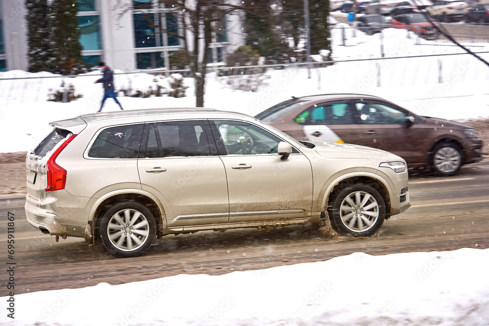 SUV rides fast on slushy winter road in the city. Car on slippery snowy road in motion. Overspeed in city, dangerous driving in winter. Car riding during blizzard. Automobile on frosty dirty road