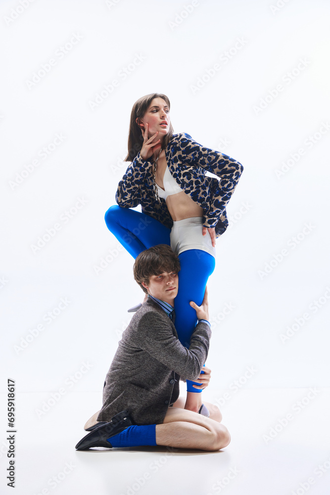Young man, half-naked guy stands on knees and hugs legs of his beloved girlfriend dressed in glamor, fashion outfit. Concept of odd romance, Valentines day, bizarre love, fashion and glamour.