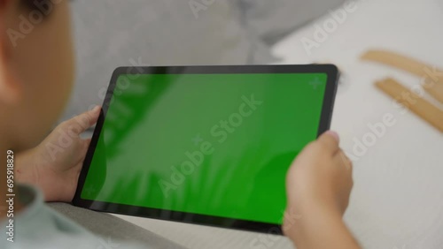 Child tilting to the left and right a tablet with green screen, side view