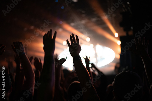 Crowd of people attending a musical performance. Putting hands up. Bright light beams coming from the stage