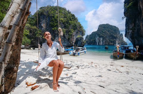 Relax vacation. Young woman swinging on teeterboard near the sea with fisshing longtail boats in Thailand. photo