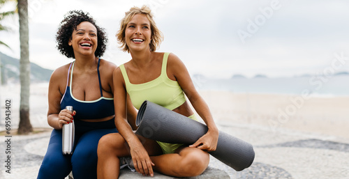 Two happy women sitting on the promenade with beach workout essentials