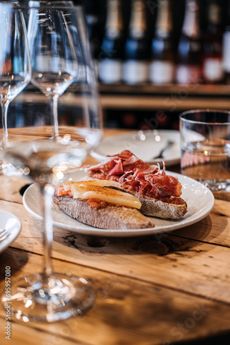 An inviting display of Spanish tapas, featuring crusty bread topped with cheese and cured ham, accompanied by elegant wine glasses on a wooden table.