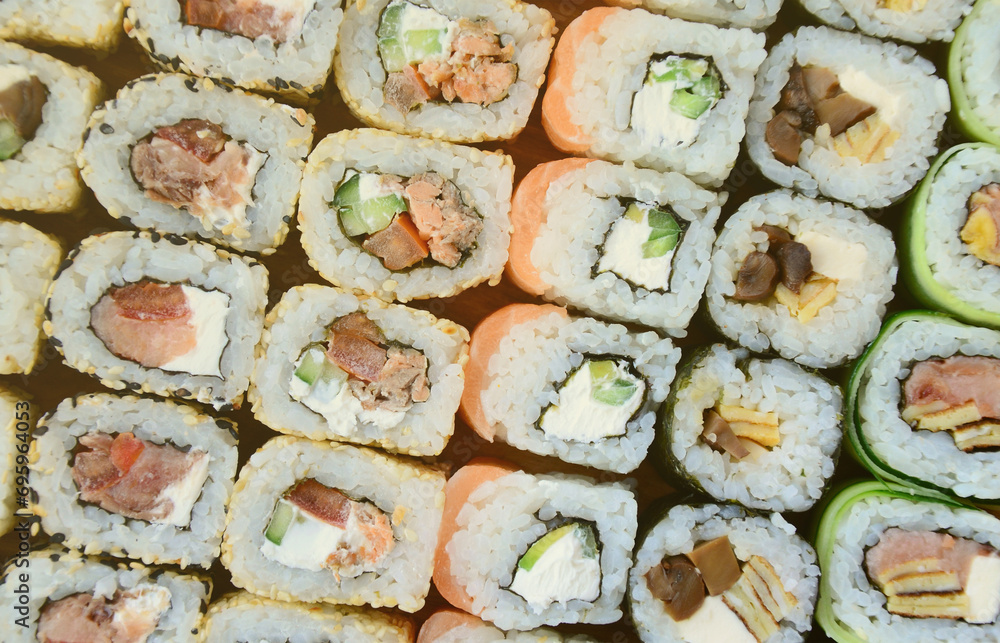 Close-up of a lot of sushi rolls with different fillings lie on a wooden surface. Macro shot of cooked classic Japanese food with a copy space. Close-up of a lot of sushi rolls with different fillings lie on a wooden surface. Macro shot of cooked classic Japanese food with a copy space.