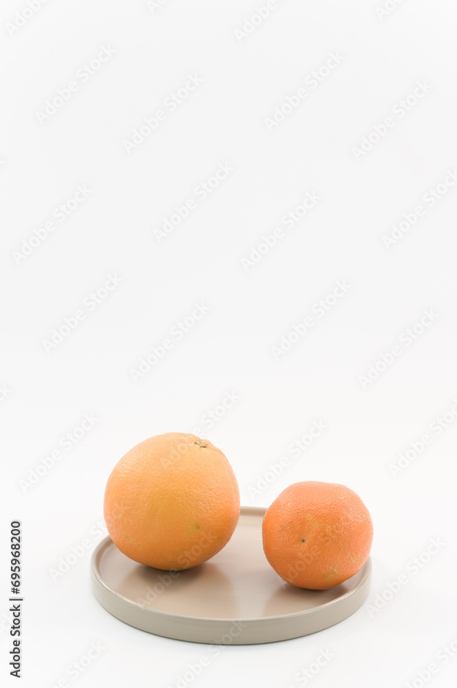 immagine con primo piano di frutti di arancia e mandarino, su piccolo piatto superficie bianca immagine con primo piano di frutti di arancia e mandarino, su piccolo piatto superficie bianca