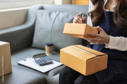 Asian woman working from home SME entrepreneurs use smartphones and laptops for commercial monitoring. Online marketing packed in a parcel box. Close-up image