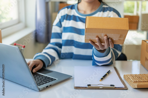 Fototapeta Naklejka Na Ścianę i Meble -  Asian woman working from home SME entrepreneurs use smartphones and laptops for commercial monitoring. Online marketing packed in a parcel box. Close-up image