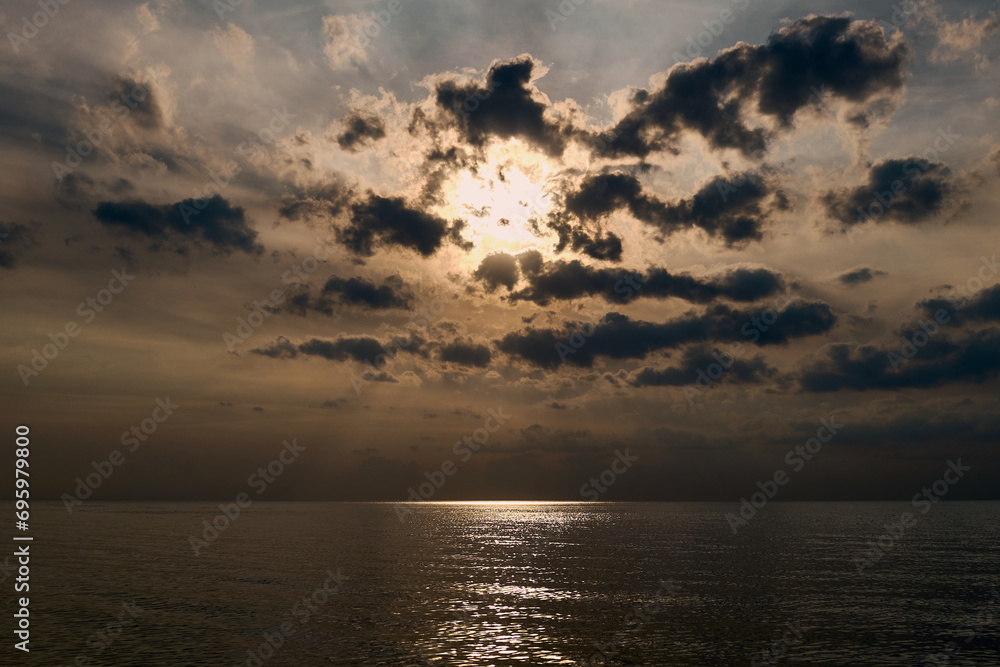 Dramatic sunset on the seaside, sun behind dark clouds, calm Baltic Sea