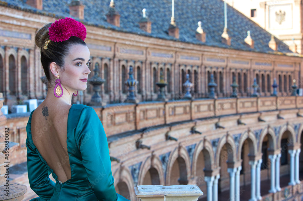 Beautiful young woman with typical green frilly dress and dancing flamenco in plaza de espana in sevilla, andalusia, she is on a balcony of the famous square. 16 november, international flamenco day.