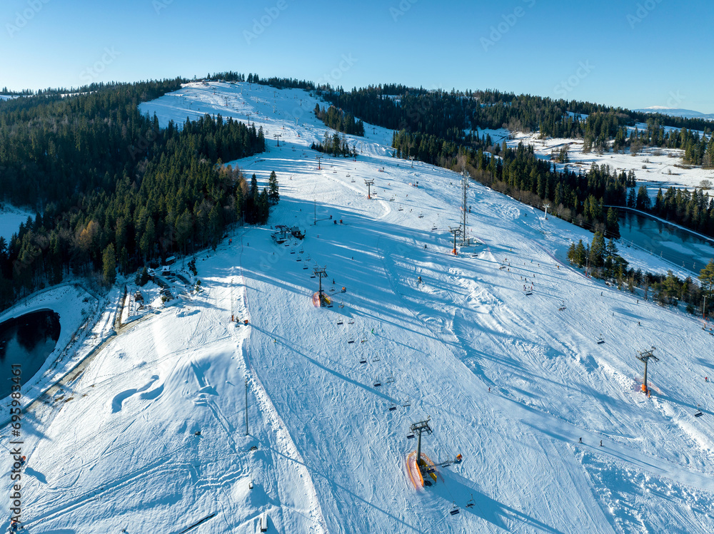 Ski slope, chairlifts, skiers and snowboarders in Bialka Tatrzanska ski resort in Poland on Kotelnica Mountain in winter. Aerial view in low December light