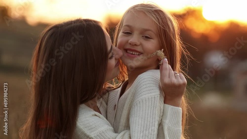 Family day, mother's day. Happy smiling young mom and adorable child daughter soft hugging, kissing and spending time together at autumn on sunset. Idyllic family having fun outdoors on fall holiday photo
