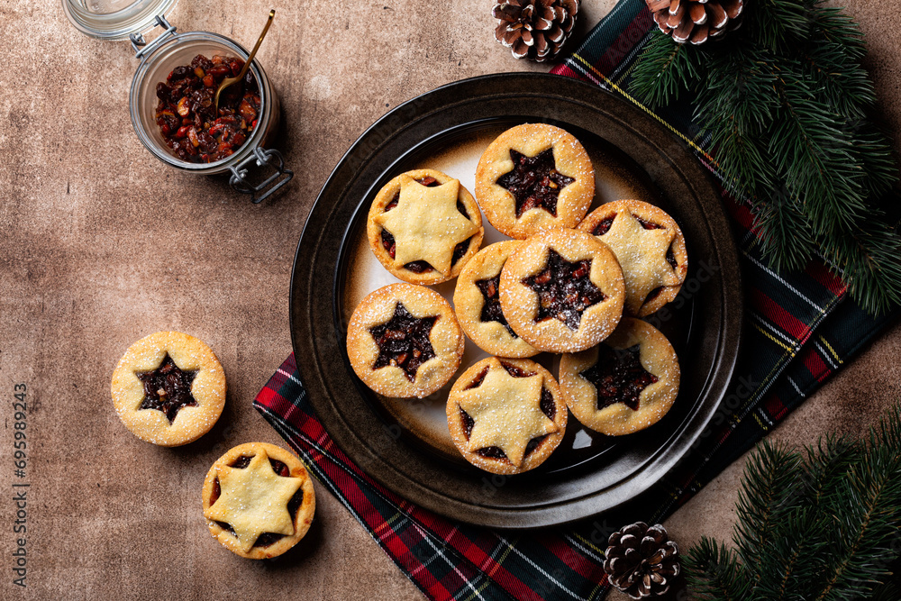 Traditional british christmas Mince pies on a brown plate, sprinkled with sugar. Also called mincemeat or fruit pie, filled with a mixture of fruit, spices and suet. Festive table, directly above. Traditional british christmas Mince pies on a brown plate, sprinkled with sugar. Also called mincemeat or fruit pie, filled with a mixture of fruit, spices and suet. Festive table, directly above.