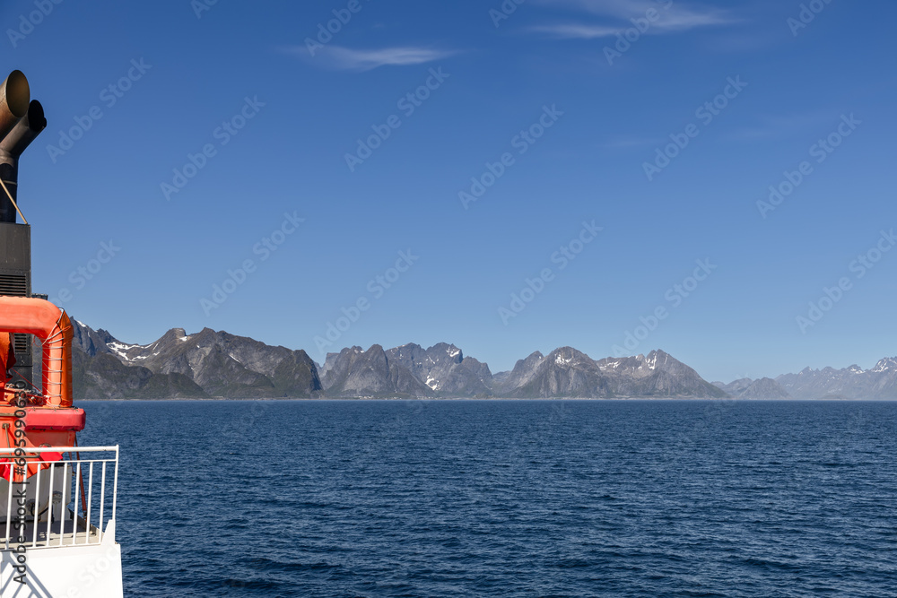 A summer perspective from a ferry on the North Sea, heading towards the Lofoten Islands, highlighting the tranquil blue sky and the striking scenery of Arctic Norway