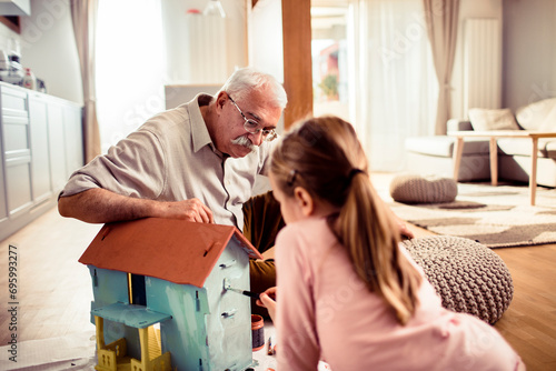Grandfather painting small toy house with granddaughter at home photo