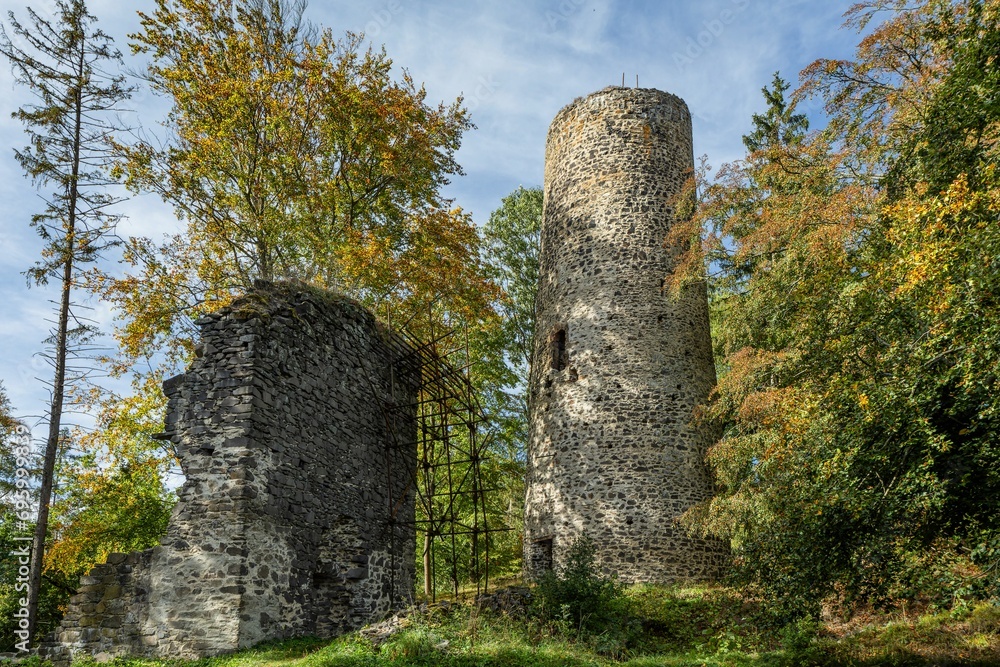 Cernosin, Czech Republic - October 13 2023: View of the ruined castle Volfstejn standing on a hill in the forest. Stone tower and the wall under reconstruction. Sunny autumn day with blue sky.