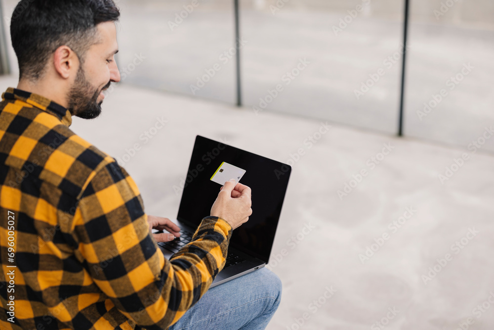 smiling young adult man with his credit card and laptop making online purchases from anywhere in the world smiling young adult man with his credit card and laptop making online purchases from anywhere in the world