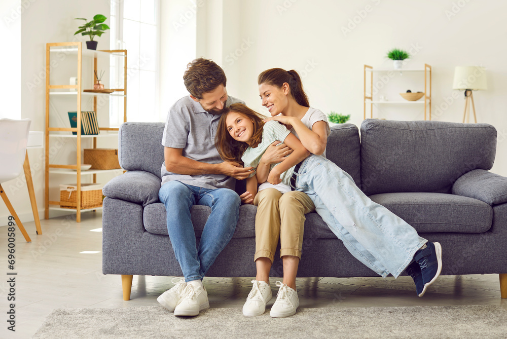 Cheerful nuclear family spending time together at home. Happy parents and child having fun together. Happy, loving mother, father and daughter sitting and hugging on the sofa in the living room