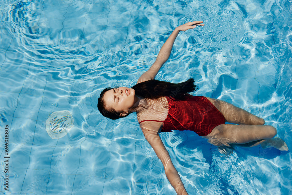 Happy woman swimming in the pool in red swimsuit with loose long hair relaxed in the sunshine, skin protection with sunscreen, concept of relaxing on vacation in tropical climate, lifestyle.