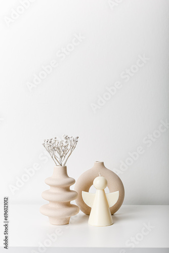 Beige ceramic small vases and candle. Cozy home. Copy space, minimalism, scandinavian decoration. Winter fairy tale. White background. Light wall. Dry garass with snow. photo