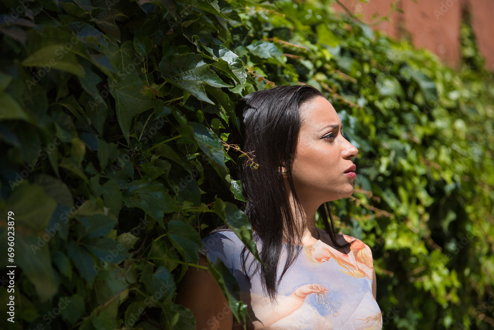 Young woman, beautiful, brunette and South American with a printed shirt, calm and relaxed on a background of green ivy, receiving the rays of the sun. Concept beauty, fashion, plants. Young woman, beautiful, brunette and South American with a printed shirt, calm and relaxed on a background of green ivy, receiving the rays of the sun. Concept beauty, fashion, plants.