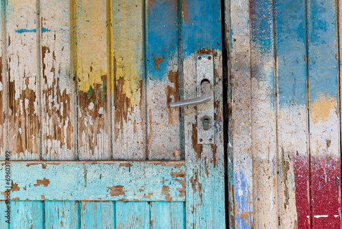 Section of a colorfully painted old door with peeling wooden boards andsilver door handle