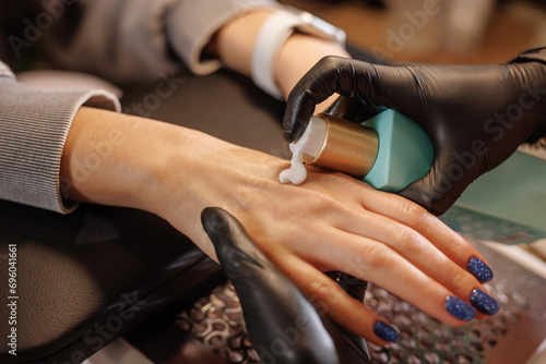 manicurist applies cream to client's hands for hand care in beauty salon